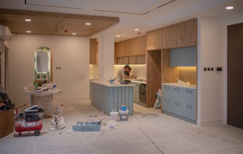 A modern kitchen undergoing renovation, featuring a worker, tools, and materials.