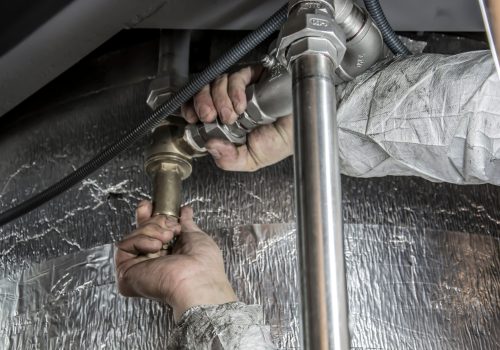 Close-up of a plumber's hands installing steel pipes indoors, showcasing skilled manual work.